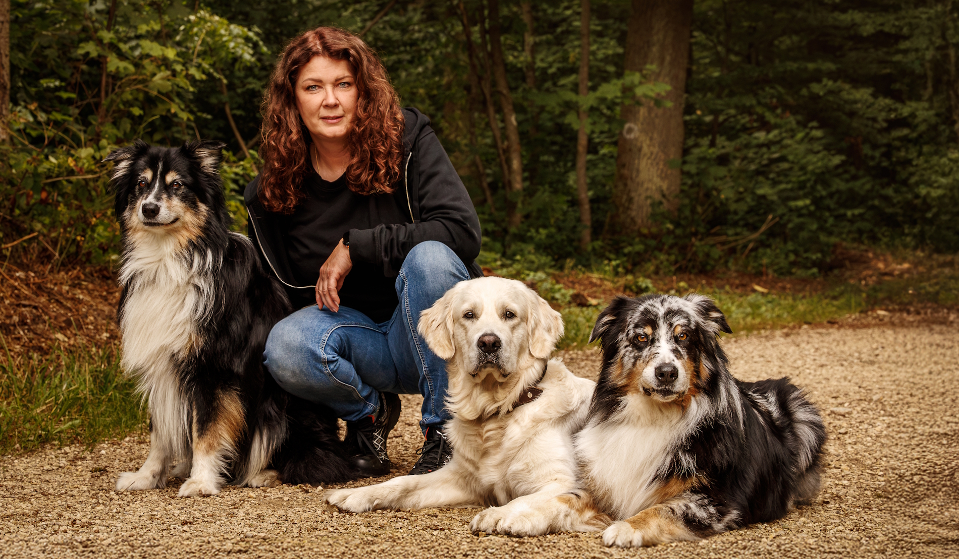Inhaberin der Hundeschule Balanced Dogwork knieend zwischen ihren beiden Hunden, die links und rechts von ihr auf einem Stuhl liegen